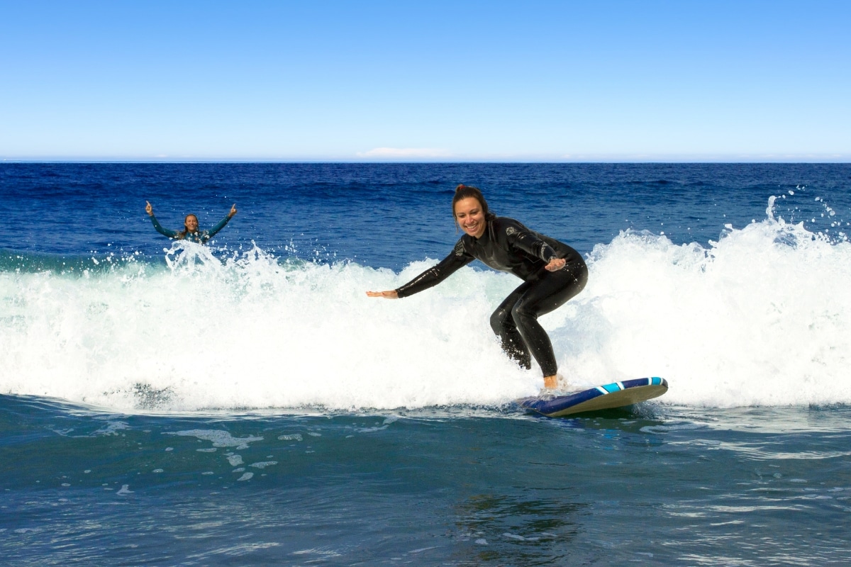 One surfer catches a wave, while another cheers in the background