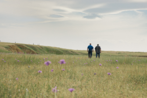 Two men walking through a grassy field.
